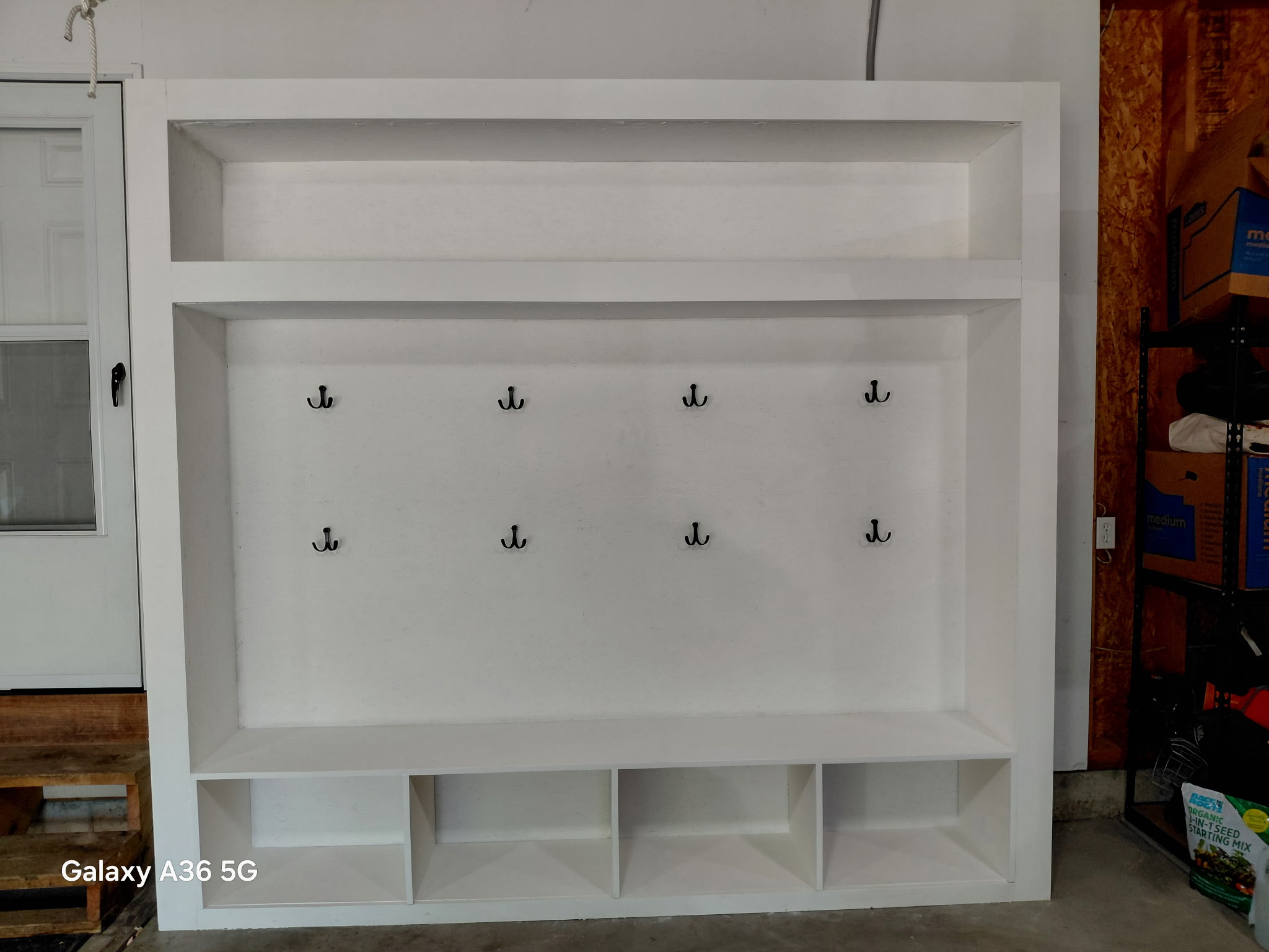 Custom white mudroom locker built-in with double coat hooks, bench seat, shoe cubbies, and upper storage shelf