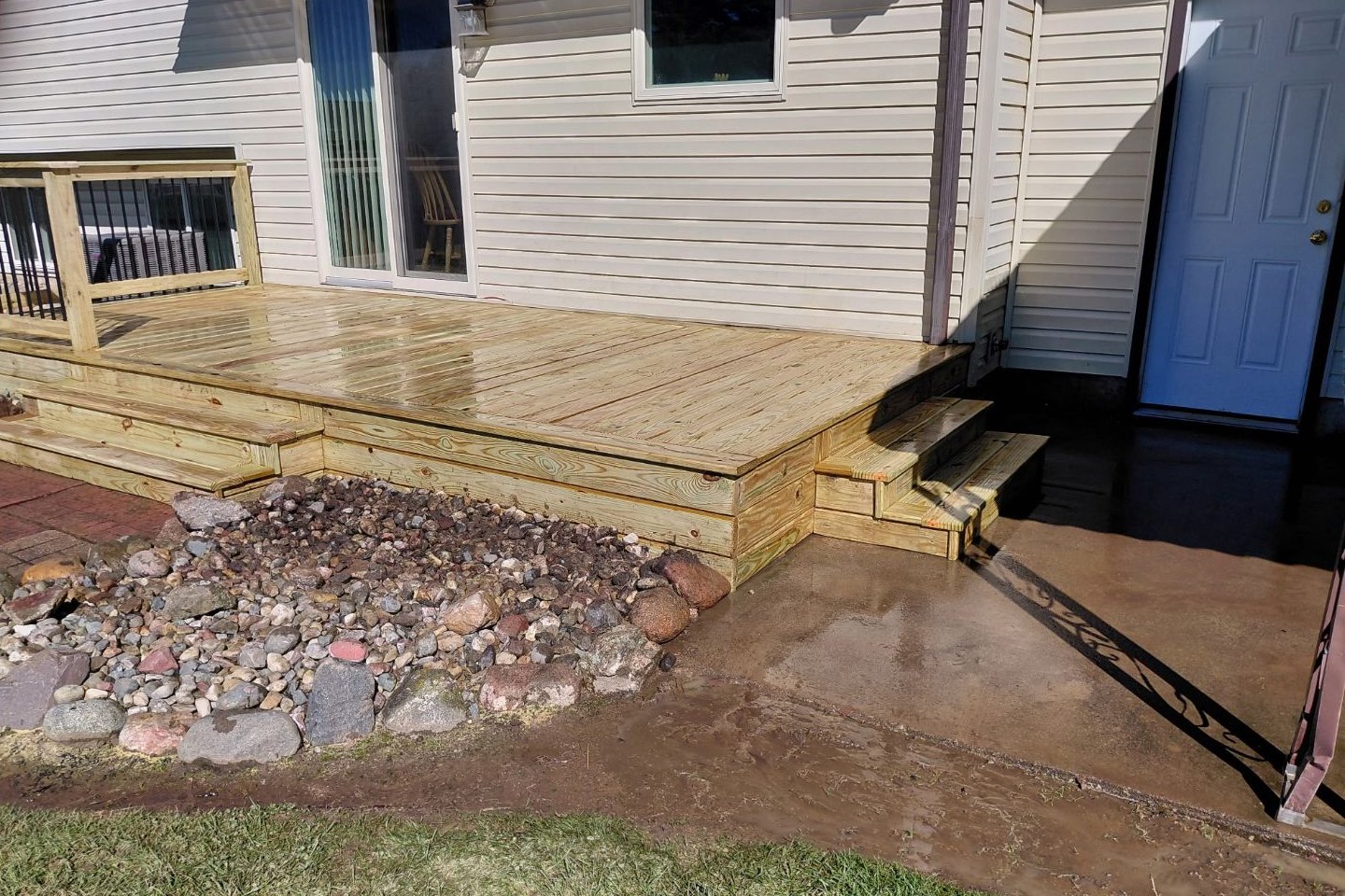 New pressure-treated backyard deck off a sliding door, with box steps down to a paver patio on one side and a concrete pad on the other