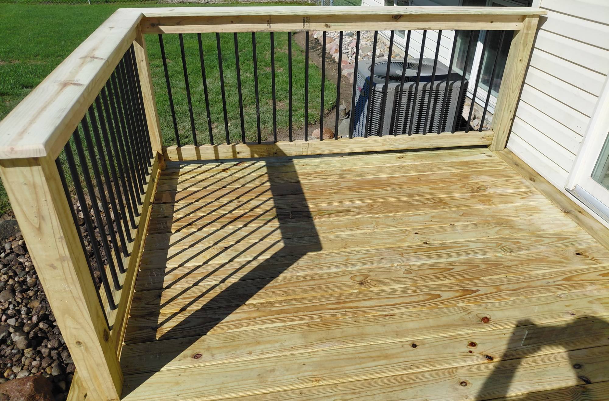 Railed corner of the deck with a flat wood cap rail and black round balusters