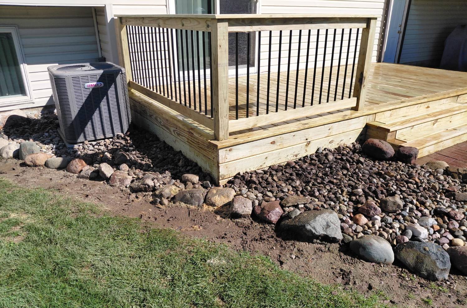 The railed corner seen from the yard, with skirt boards running down to the stone border beside the air conditioner